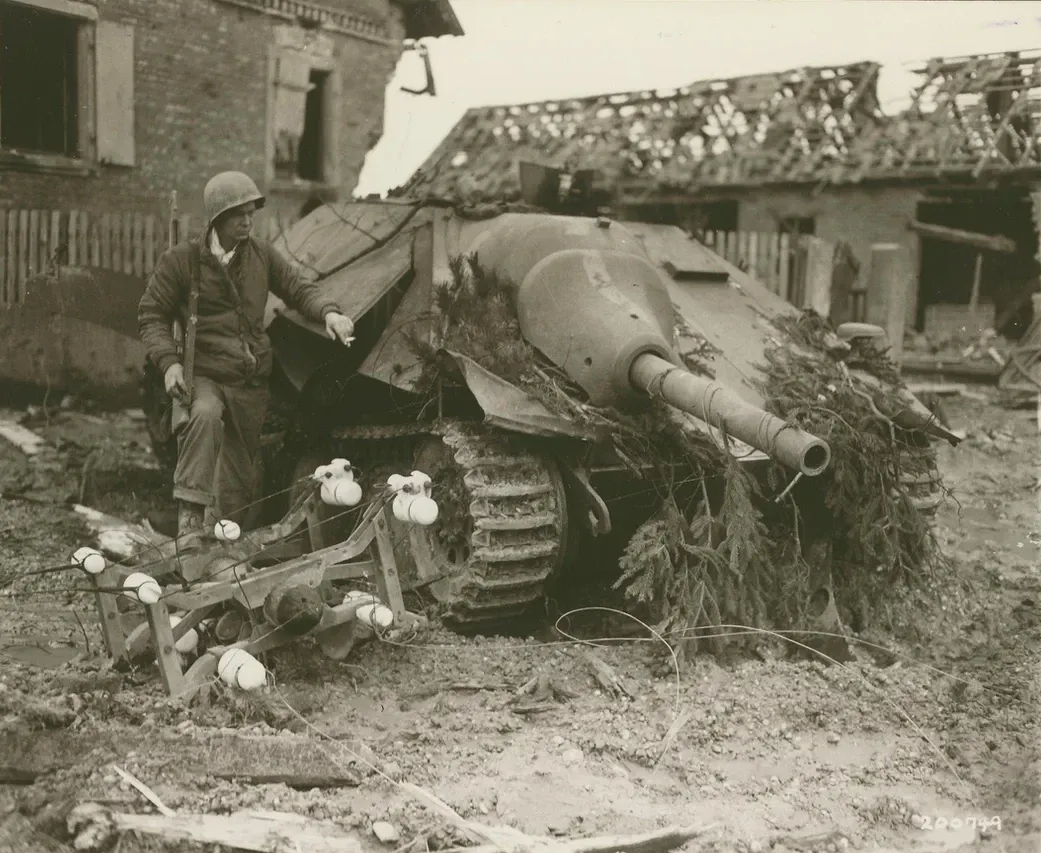 Man standing next to a destroyed German Hetzer tank destroyer